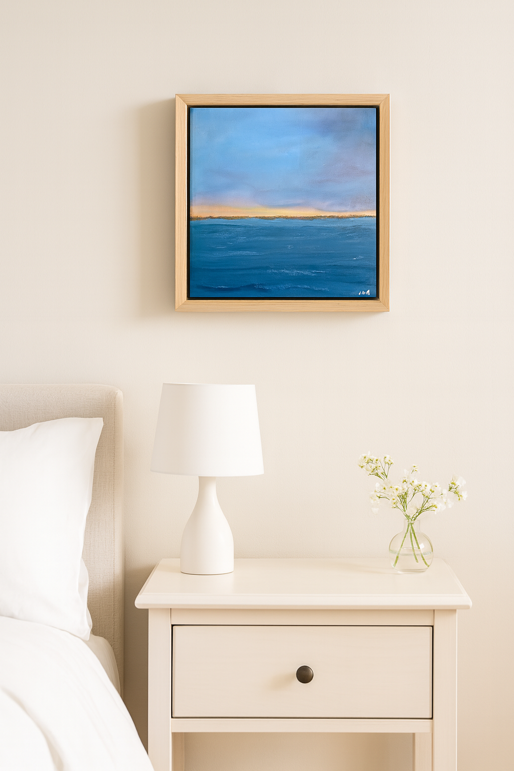 Framed artwork on a wall above a nightstand with a lamp and vase.